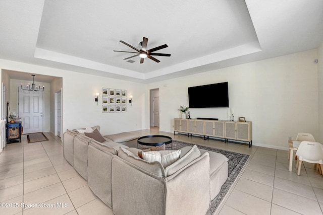 living area featuring light tile patterned floors, a tray ceiling, baseboards, and ceiling fan with notable chandelier