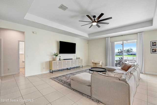 living area featuring visible vents, ceiling fan, a tray ceiling, light tile patterned floors, and a textured ceiling