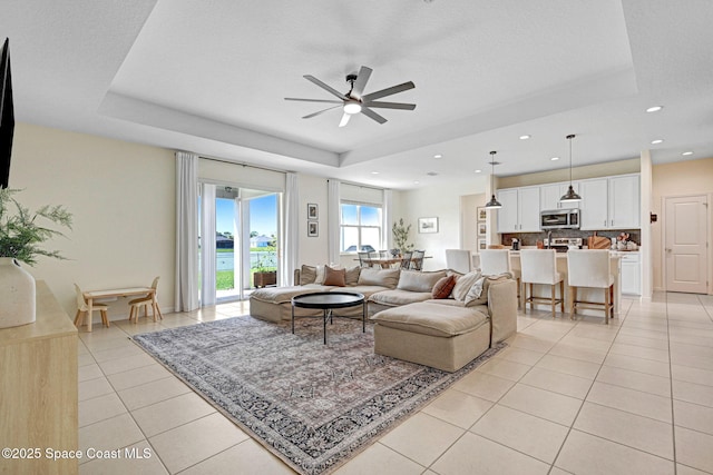 living room featuring light tile patterned floors, a tray ceiling, ceiling fan, and recessed lighting