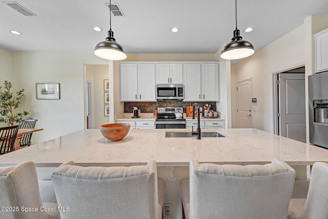kitchen featuring tasteful backsplash, visible vents, appliances with stainless steel finishes, white cabinetry, and a sink