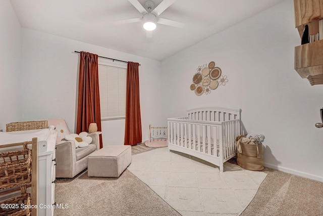 bedroom featuring a nursery area, light colored carpet, baseboards, and ceiling fan