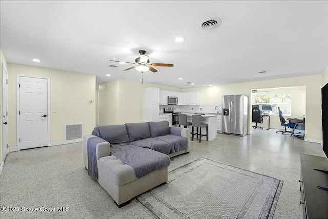 living area featuring light speckled floor, a ceiling fan, and visible vents