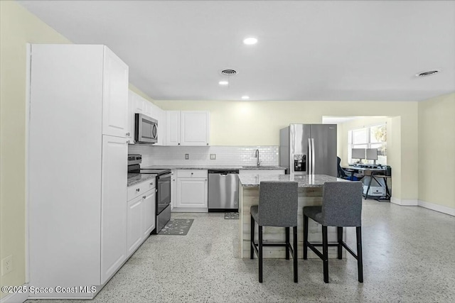 kitchen with a breakfast bar, decorative backsplash, stainless steel appliances, white cabinetry, and a sink