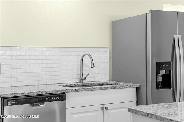 kitchen with a sink, appliances with stainless steel finishes, white cabinets, decorative backsplash, and light stone countertops