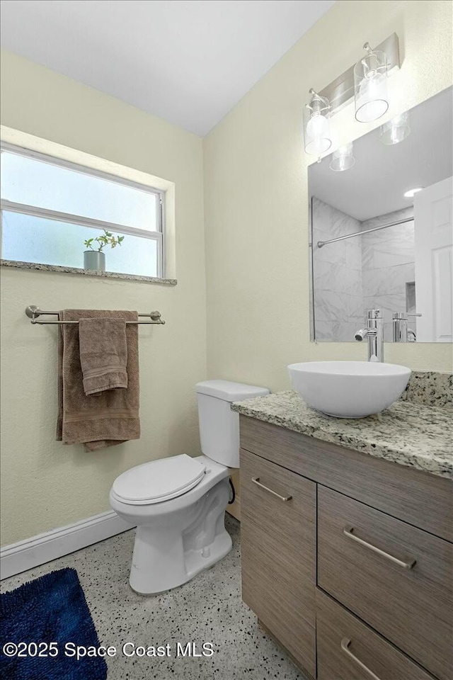 bathroom with toilet, a shower, speckled floor, baseboards, and vanity