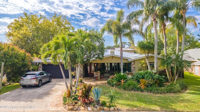 mid-century modern home featuring stucco siding, concrete driveway, a front lawn, a garage, and metal roof