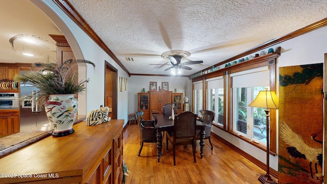 dining room featuring baseboards, ceiling fan, ornamental molding, light wood-style floors, and a textured ceiling