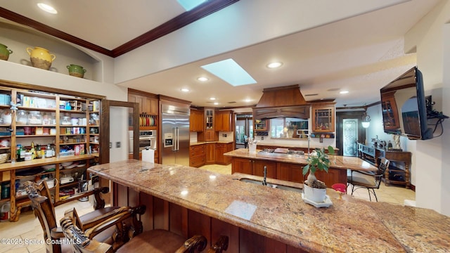 kitchen featuring premium range hood, brown cabinets, ornamental molding, a breakfast bar area, and a skylight