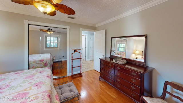 bedroom featuring a textured ceiling, ornamental molding, visible vents, and light wood-type flooring