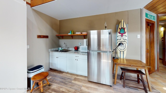 kitchen featuring white microwave, a sink, freestanding refrigerator, white cabinets, and open shelves