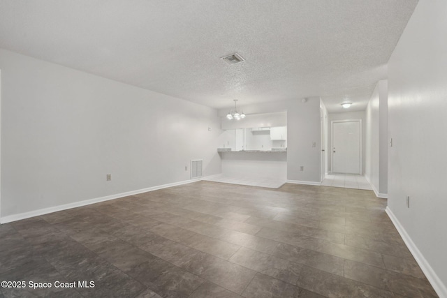 unfurnished living room with visible vents, baseboards, a textured ceiling, and an inviting chandelier