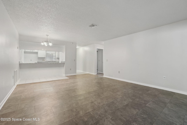 unfurnished living room featuring an inviting chandelier, baseboards, visible vents, and a textured ceiling