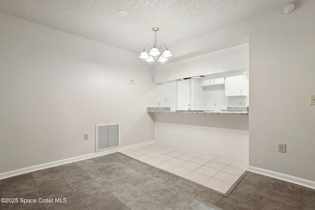 interior space with a chandelier, visible vents, a textured ceiling, and baseboards