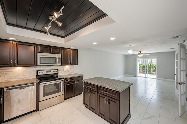 kitchen featuring a tray ceiling, stainless steel appliances, tasteful backsplash, and marble finish floor