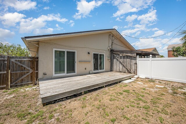 rear view of house featuring stucco siding, a gate, fence, and a wooden deck