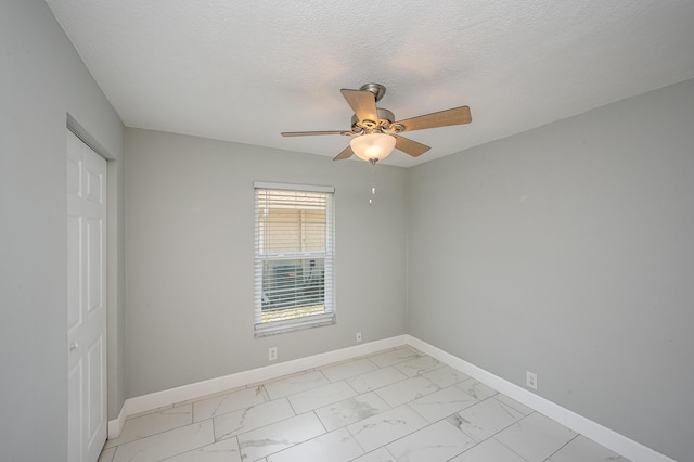 spare room featuring marble finish floor, a textured ceiling, baseboards, and a ceiling fan