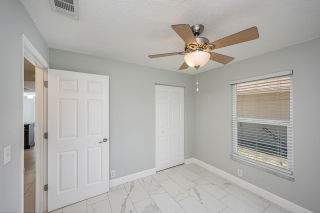 unfurnished bedroom with visible vents, baseboards, a closet, a textured ceiling, and marble finish floor