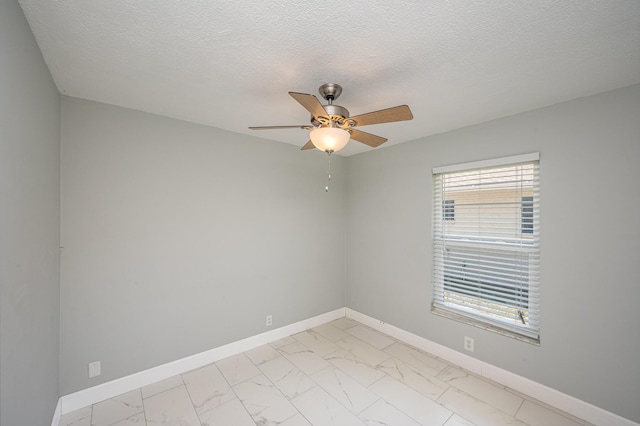 empty room with a ceiling fan, baseboards, marble finish floor, and a textured ceiling