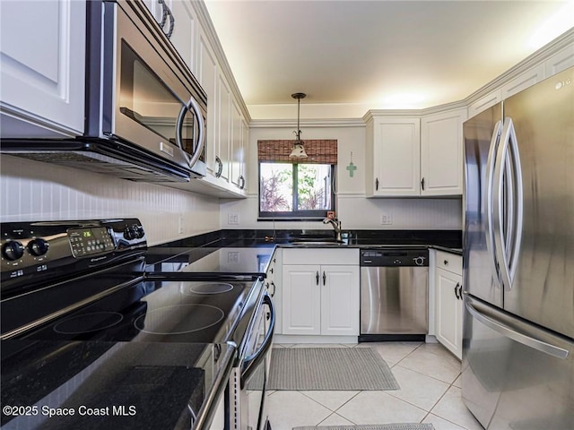 kitchen featuring dark countertops, light tile patterned flooring, white cabinets, stainless steel appliances, and a sink