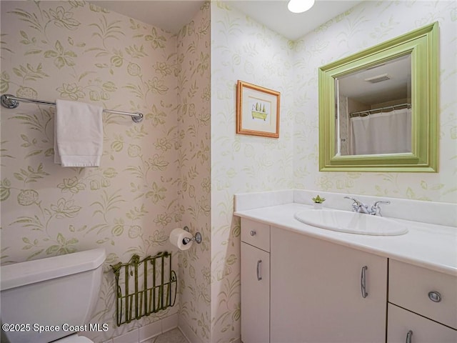 bathroom with wallpapered walls, toilet, vanity, and visible vents