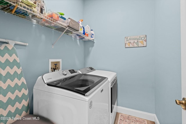 clothes washing area with baseboards, separate washer and dryer, and laundry area