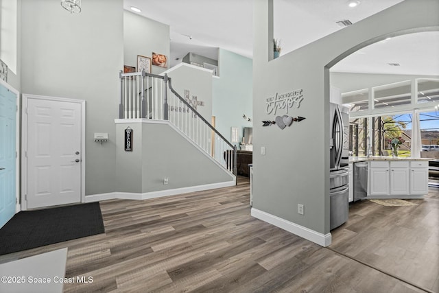 entryway featuring wood finished floors, stairway, arched walkways, a high ceiling, and baseboards