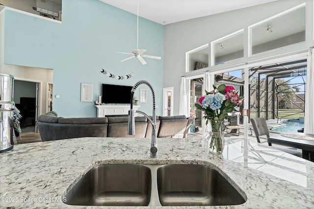 kitchen featuring a ceiling fan, light stone countertops, a sink, a towering ceiling, and open floor plan