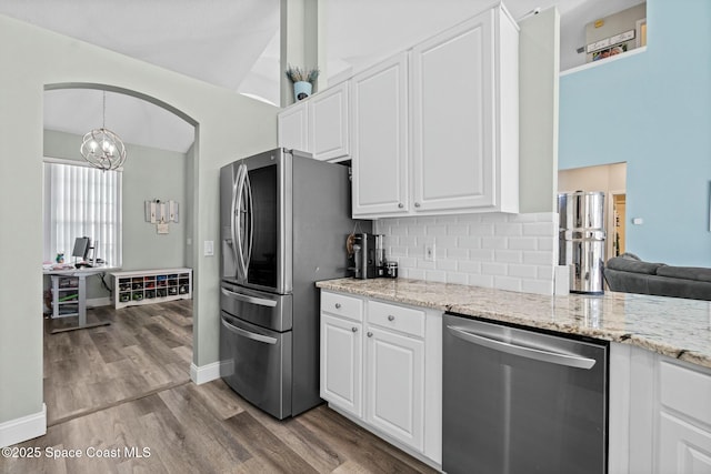 kitchen featuring wood finished floors, light stone countertops, stainless steel appliances, white cabinetry, and tasteful backsplash