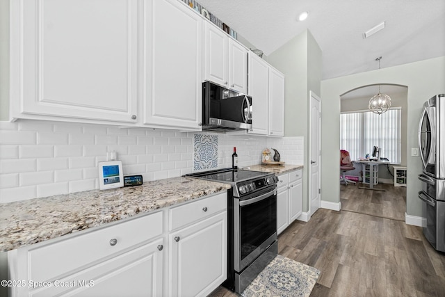 kitchen with arched walkways, backsplash, appliances with stainless steel finishes, and white cabinetry