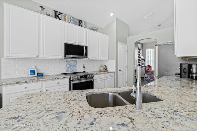 kitchen with arched walkways, backsplash, appliances with stainless steel finishes, and light stone countertops