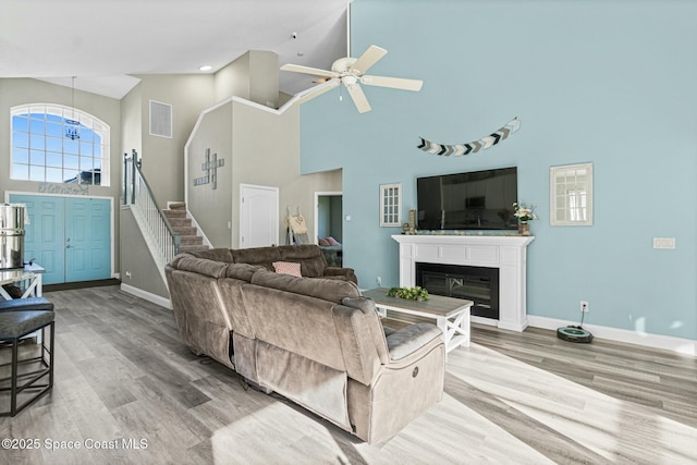 living area with wood finished floors, baseboards, ceiling fan, stairs, and a glass covered fireplace