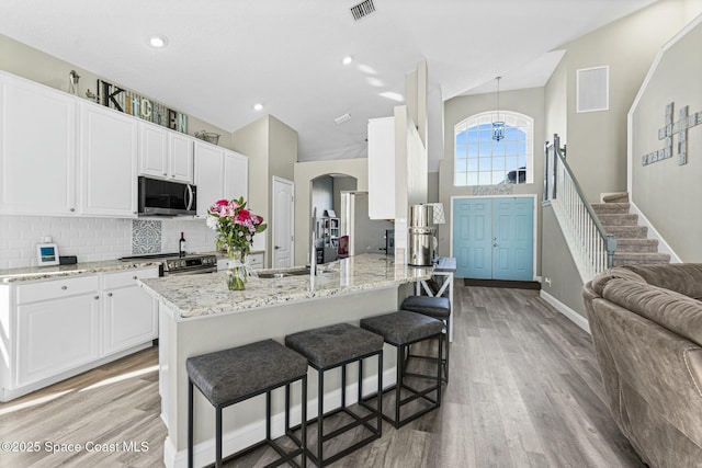 kitchen featuring visible vents, stainless steel electric stove, white cabinetry, arched walkways, and light wood finished floors