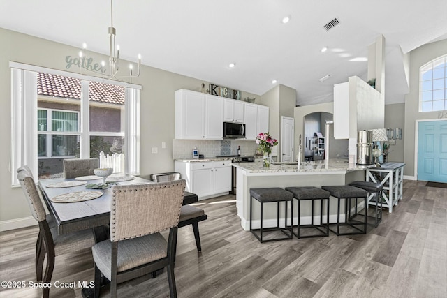 kitchen featuring stainless steel microwave, tasteful backsplash, arched walkways, light wood-style floors, and white cabinets