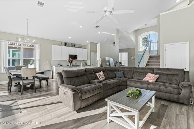 living area with visible vents, light wood-type flooring, stairs, and high vaulted ceiling