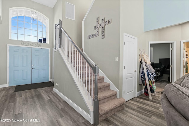 entryway with visible vents, baseboards, a towering ceiling, wood finished floors, and a notable chandelier