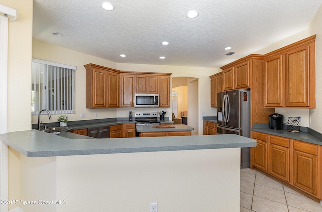 kitchen with brown cabinets, a sink, arched walkways, appliances with stainless steel finishes, and light tile patterned flooring