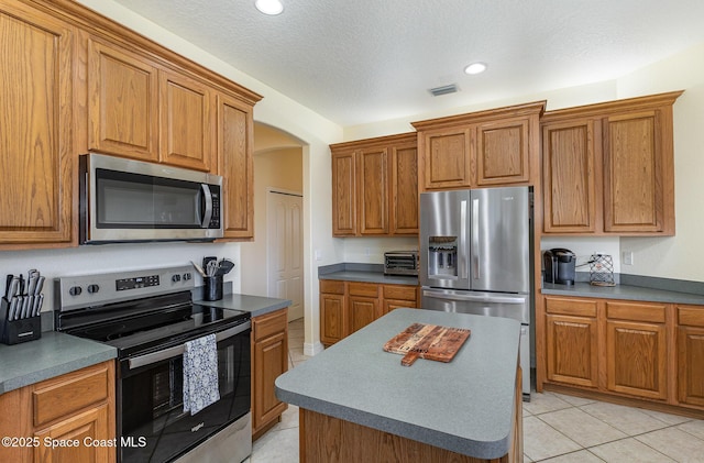 kitchen featuring light tile patterned flooring, arched walkways, brown cabinets, and stainless steel appliances