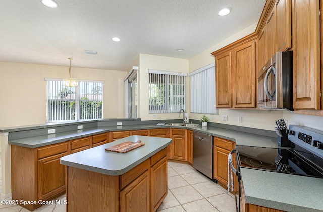 kitchen featuring light tile patterned floors, appliances with stainless steel finishes, a peninsula, brown cabinetry, and a sink