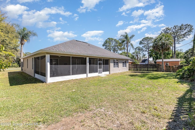 back of property with a sunroom, a lawn, a shingled roof, and fence