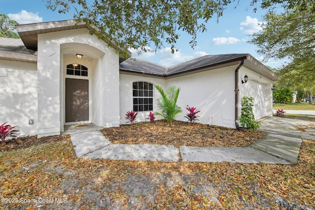 property entrance with stucco siding, an attached garage, and concrete driveway