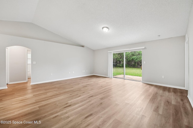 spare room featuring baseboards, light wood-type flooring, lofted ceiling, arched walkways, and a textured ceiling