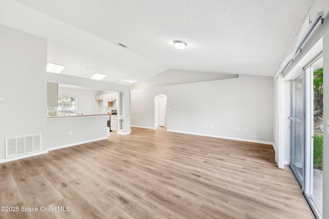 unfurnished living room featuring a wealth of natural light, visible vents, light wood-style floors, and vaulted ceiling