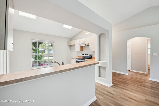 kitchen featuring a peninsula, arched walkways, vaulted ceiling, electric stove, and under cabinet range hood