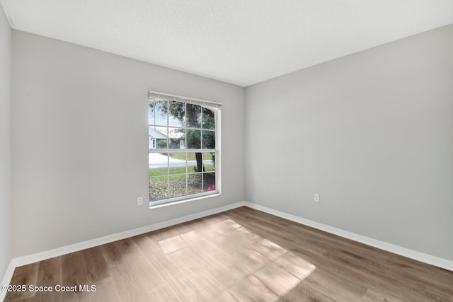 spare room with a textured ceiling, baseboards, and wood finished floors