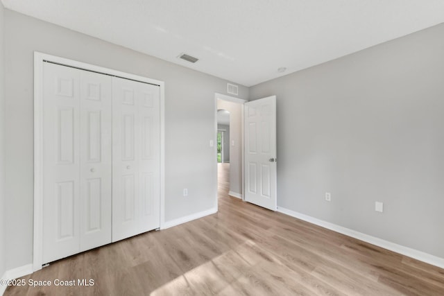 unfurnished bedroom featuring visible vents, baseboards, a closet, and wood finished floors