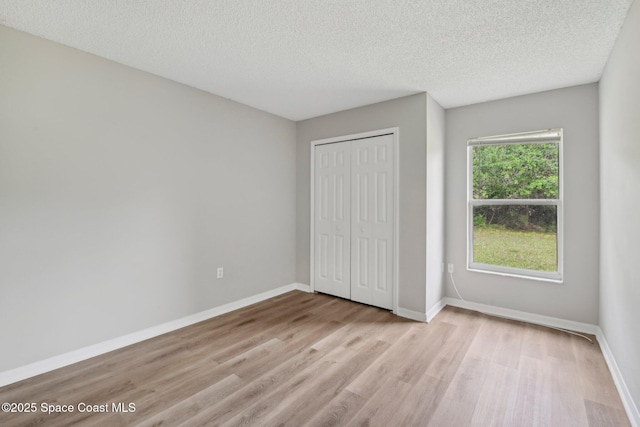 unfurnished bedroom with a closet, a textured ceiling, light wood-style floors, and baseboards