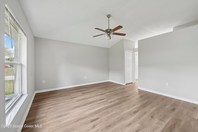 empty room featuring ceiling fan, baseboards, light wood-style floors, and lofted ceiling