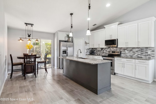 kitchen with a sink, light stone counters, stainless steel appliances, decorative backsplash, and lofted ceiling