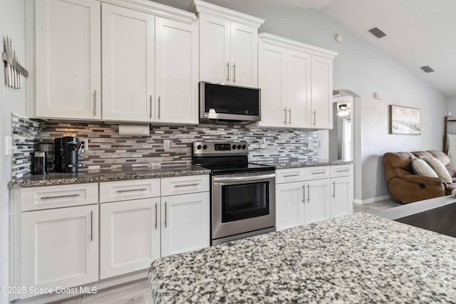 kitchen featuring lofted ceiling, stainless steel appliances, arched walkways, stone countertops, and white cabinetry