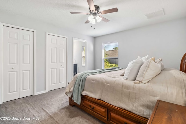 bedroom with a ceiling fan, visible vents, carpet floors, and multiple closets